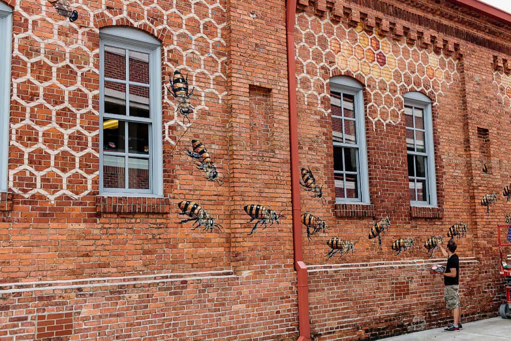 Man painting bee mural on brick building